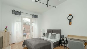 A modern bedroom with a bed, bedside tables, a desk, and a clock on the wall.