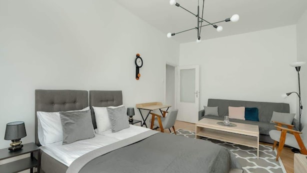 A modern bedroom with a large bed, a desk, a sofa, and a chandelier.