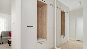 Un armario moderno blanco con estantes y cajones de madera, un sofá gris y una alfombra de tonos claros en una habitación bien iluminada.