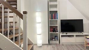 A modern living room with a staircase, a bookshelf, a flat-screen TV, and a toy train display. - Design Apartment in Carolinensiel (Wittmund)