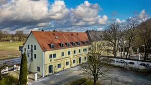 A large, single-story building with a sloped roof, multiple windows, and a sign indicating it is a business establishment. - Tafernwirtschaft Hotel Schönbrunn (Landshut)