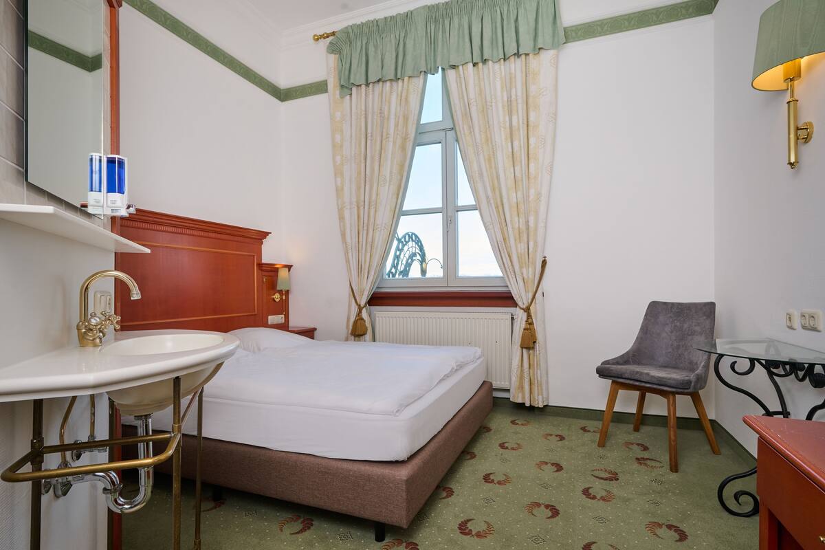 Une chambre d’hôtel avec un lit, un lavabo, une chaise et une fenêtre avec des rideaux.