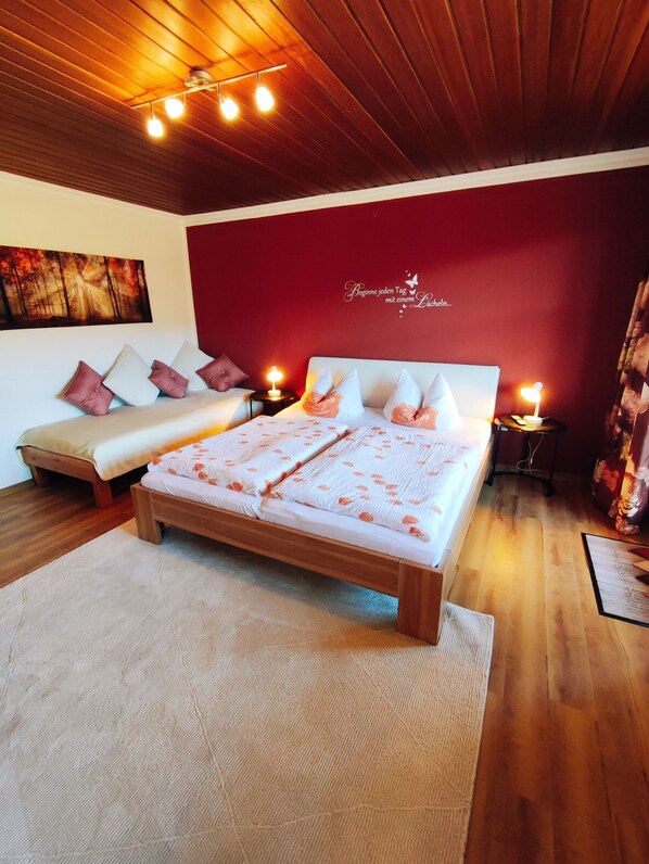 Un dormitorio con una cama de madera, una pared de acento roja, y un techo con vigas y luces a la vista.