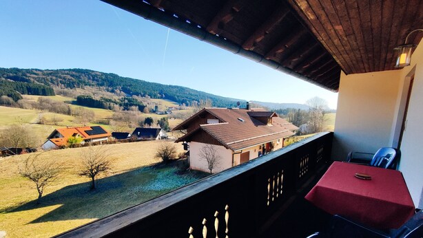 A balcony with a table and chairs, overlooking a rural landscape with houses and trees.