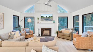A spacious living room with high ceilings, large windows, and a fireplace.
