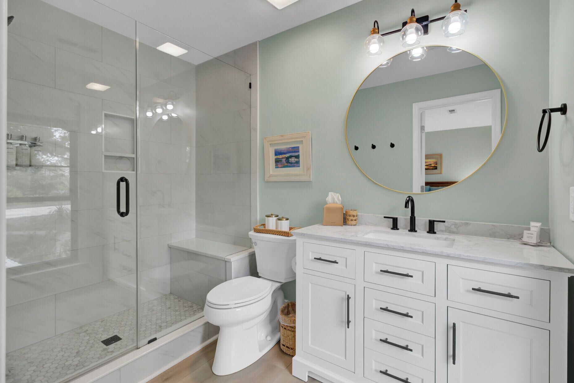 Une salle de bain moderne avec une douche à parois de verre, des toilettes blanches, un meuble-lavabo avec un miroir rond et un évier.