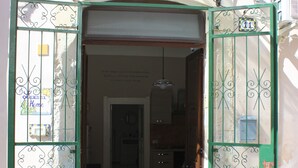 An open gate leading to a building with a visible door and a staircase.