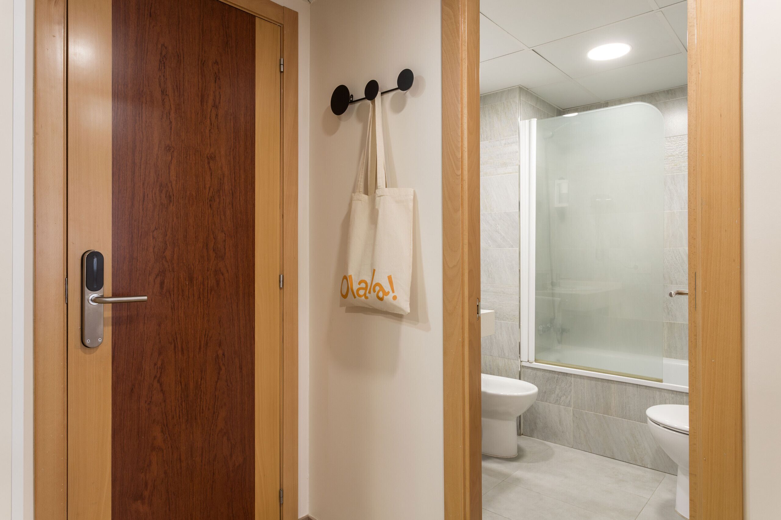 A wooden door with a modern handle, a towel rack with a white towel, and a glass shower enclosure in a bathroom.