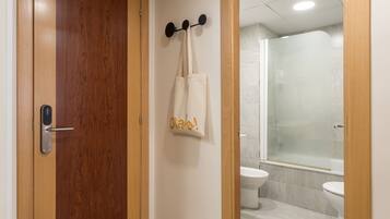 A wooden door with a modern handle, a towel rack with a white towel, and a glass shower enclosure in a bathroom.