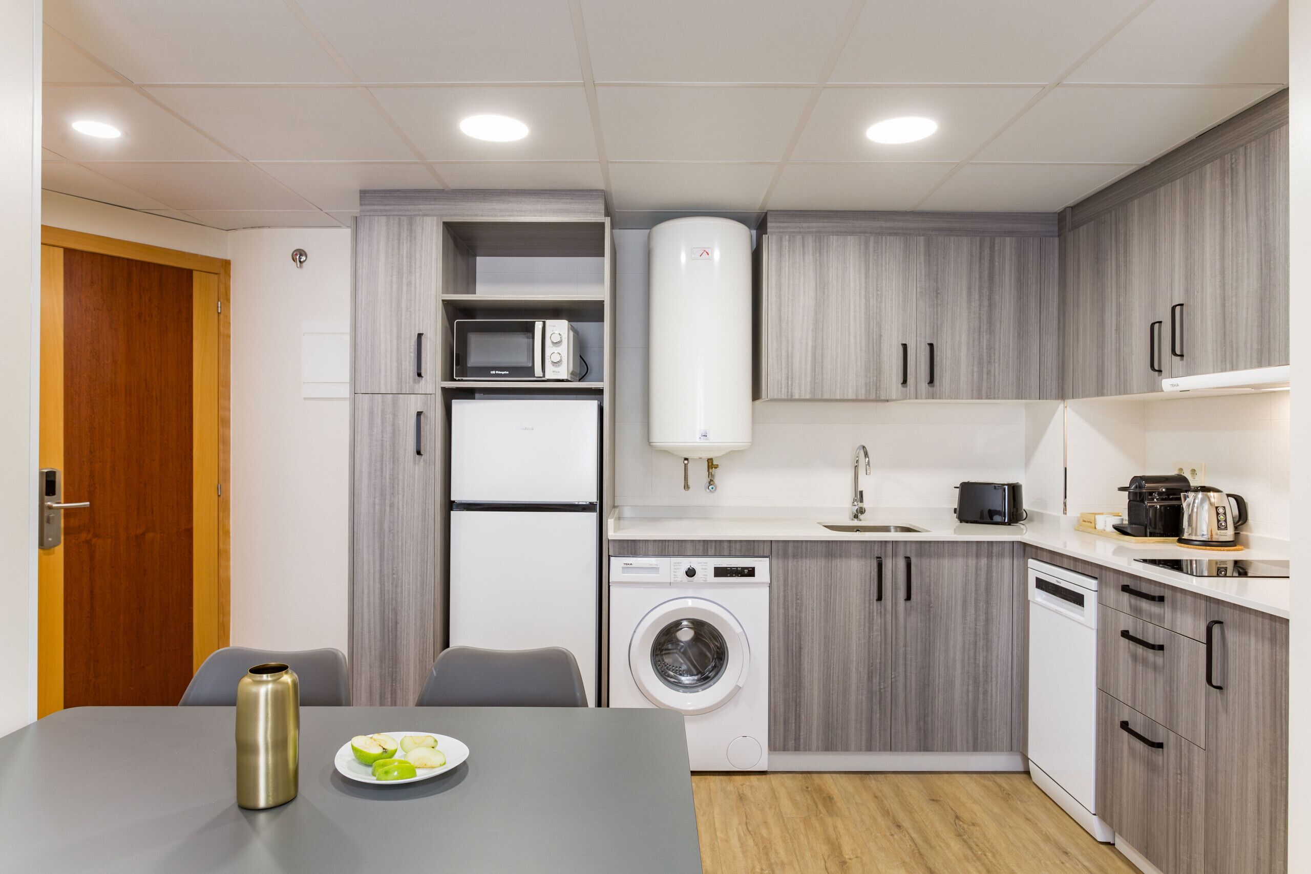 A compact kitchen with a washing machine, microwave, and a coffee maker.