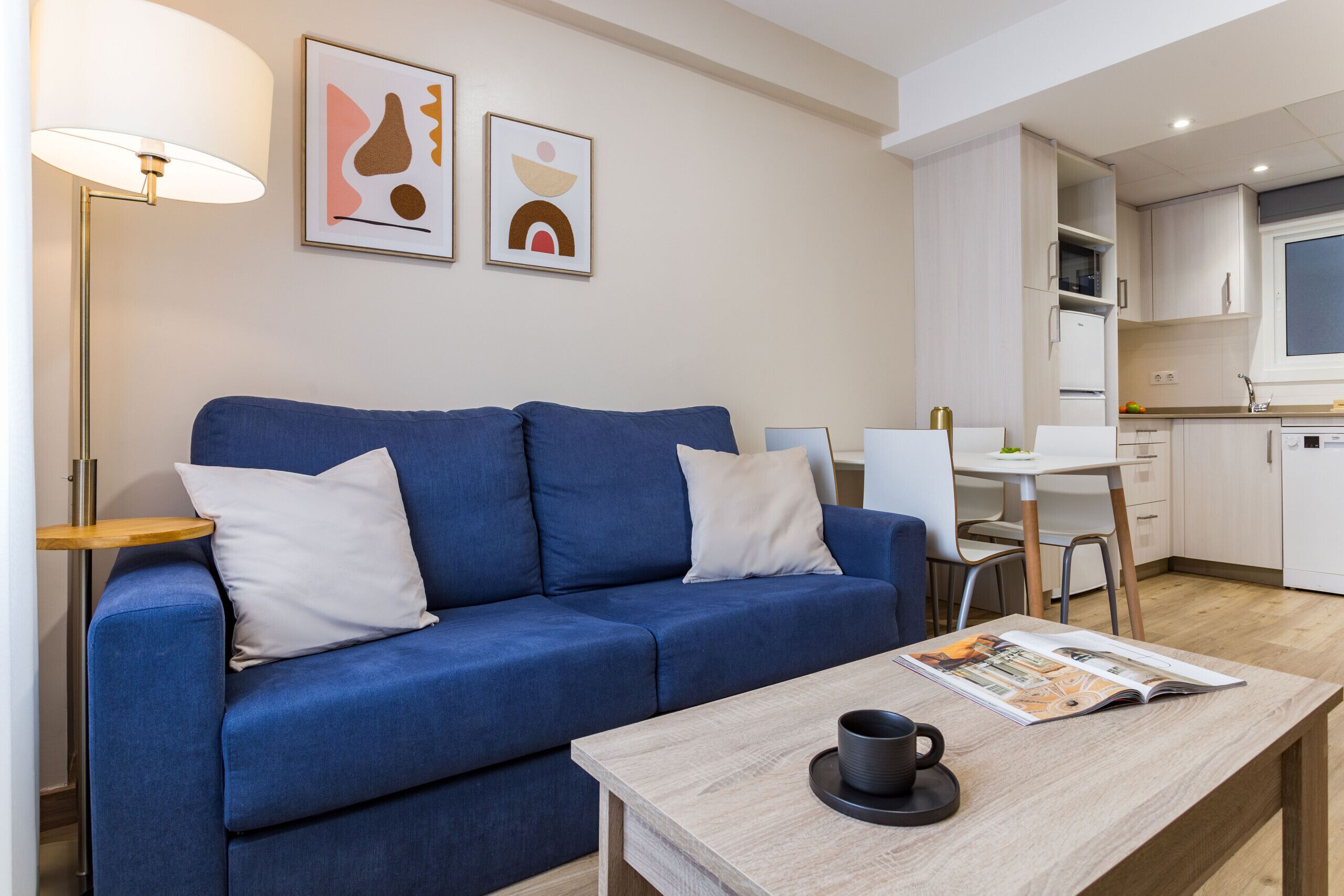 Un salon moderne avec un canapé bleu, une table basse sur laquelle se trouve un magazine et une lampe.