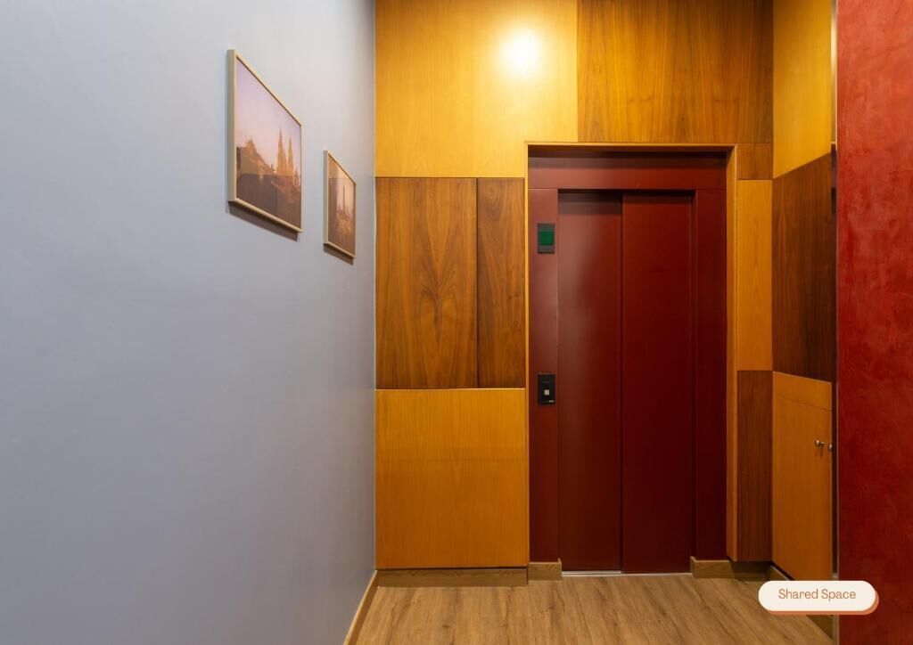 Um elevador com acabamento em madeira e porta vermelha, ladeado por paredes claras e painéis de madeira.