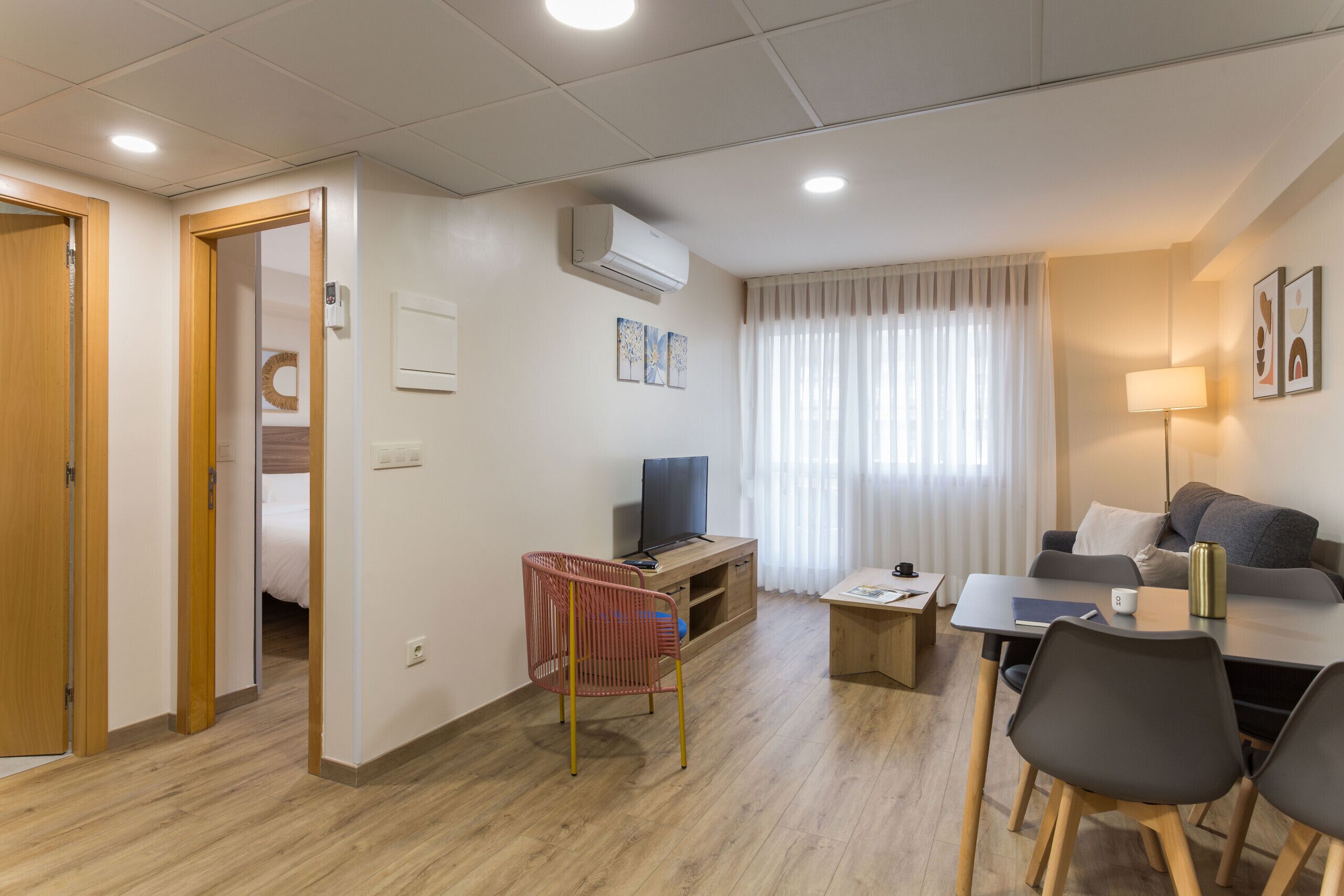 Ein modernes Hotelzimmer mit Holzboden, einem Fernseher auf einem Holztisch, einem Schreibtisch mit Stuhl, einer Couch und einer Lampe.
