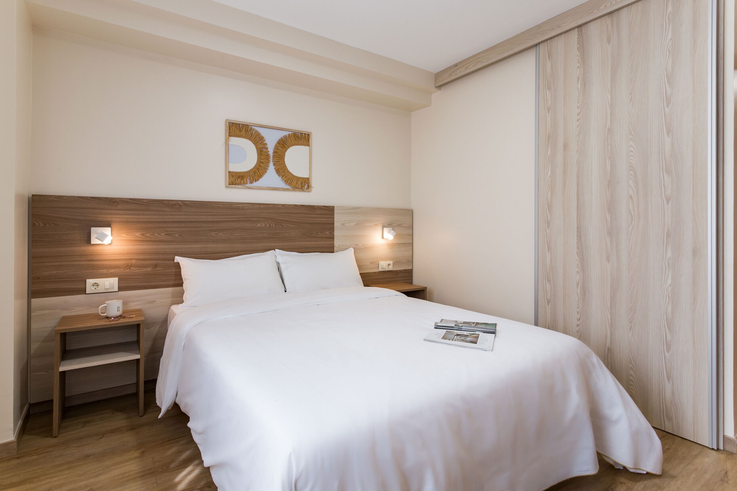 A neatly made bed with white linens, a wooden headboard, bedside tables with lamps, and a wall-mounted artwork.