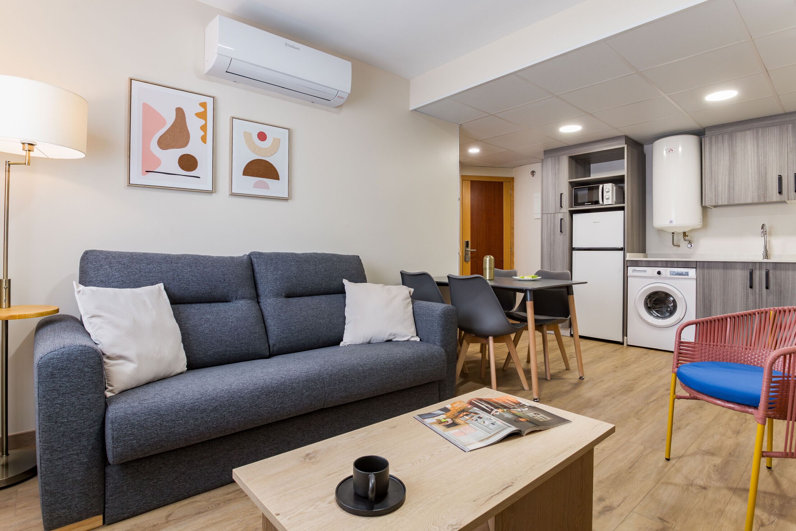 Una sala de estar moderna con un sofá gris, una mesa de centro y una zona de comedor con sillas.