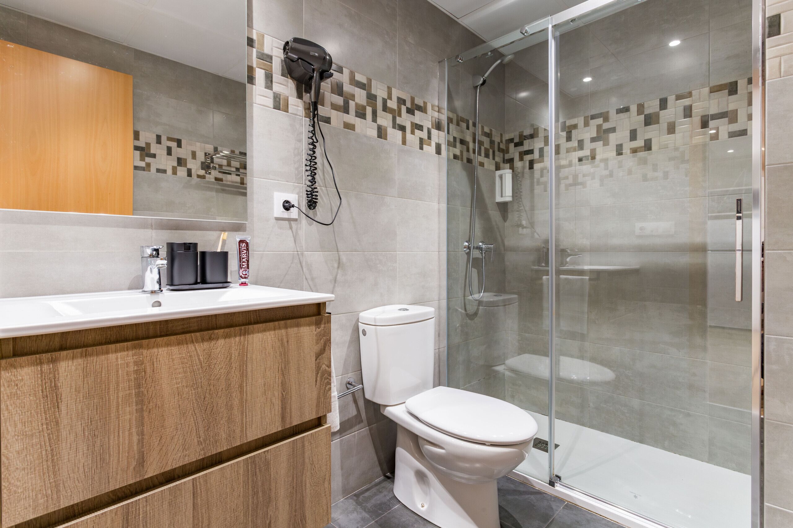 A modern bathroom with a wooden vanity, a toilet, and a glass-enclosed shower area.