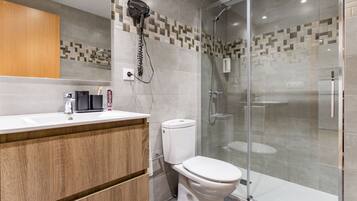 A modern bathroom with a wooden vanity, a toilet, and a glass-enclosed shower area.