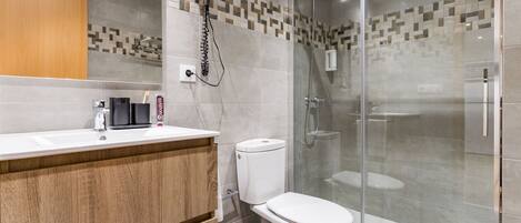 A modern bathroom with a wooden vanity, a toilet, and a glass-enclosed shower area.