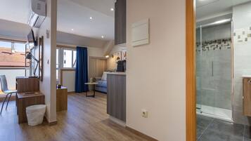 Una moderna camera d'hotel con una scrivania in legno, un piccolo angolo salotto, una doccia con pareti in vetro e vista esterna.