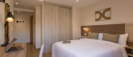 Habitación de hotel con cama, escritorio con una computadora portátil, silla y puerta que da a otra habitación.