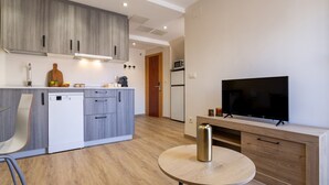 Una cocina moderna con armarios grises, un lavavajillas blanco, un microondas y un televisor sobre un soporte de madera.