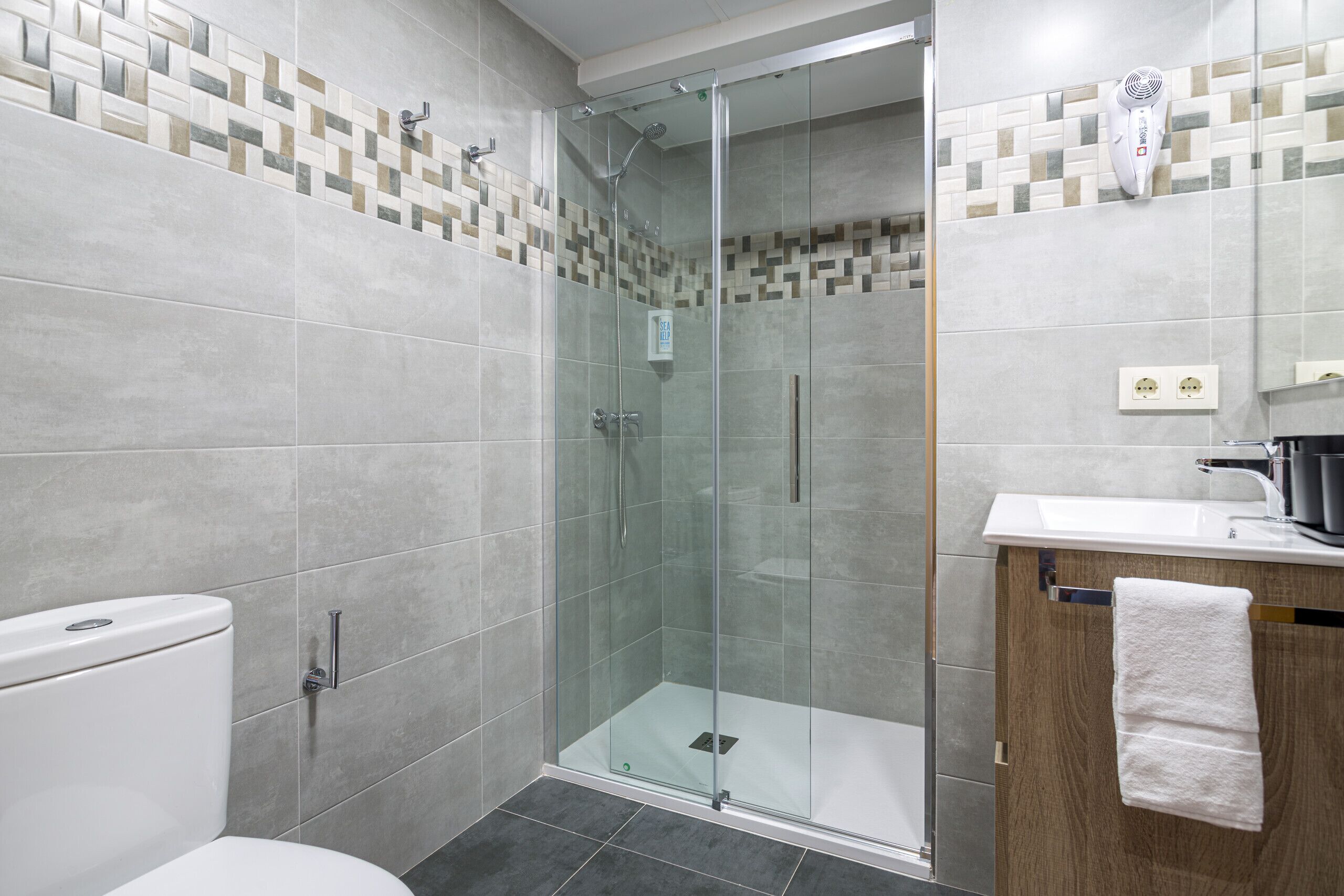 A modern bathroom with a glass-enclosed shower, a toilet, and a sink with a towel hanging on the wall.