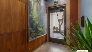 Un pasillo con un gran mural de un bosque, un cartel con la palabra 'SALIDA' y una etiqueta que indica 'Espacio Compartido'.