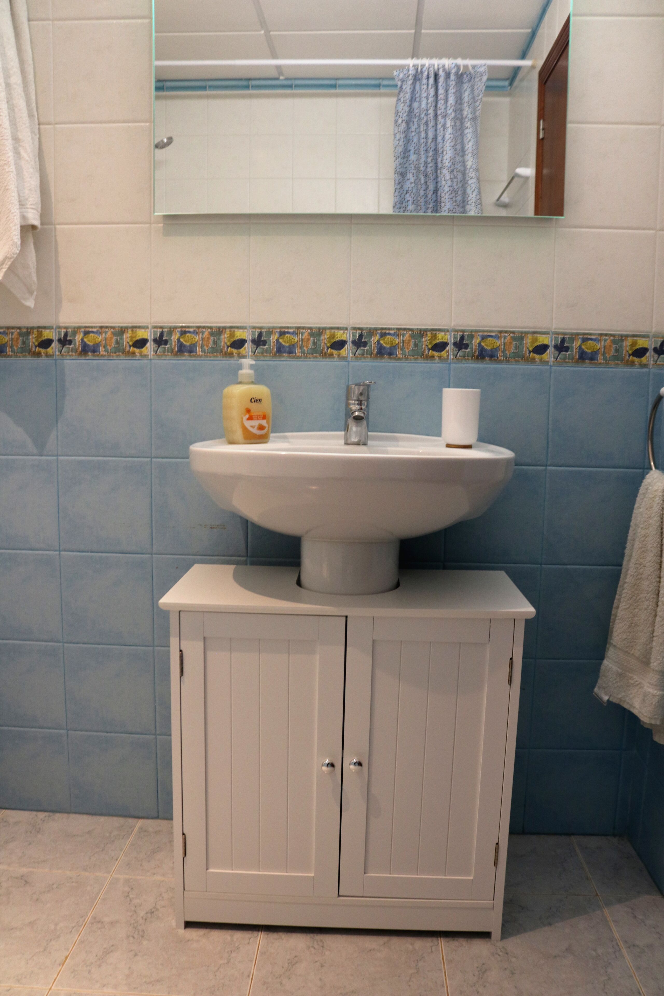 Een badkamer met een witte wastafel, een spiegel erboven en een kast eronder.