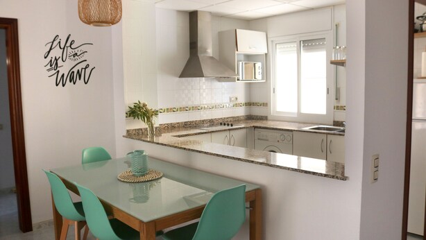 A modern kitchen with a glass dining table, teal chairs, and a kitchen island. - Tranquilidad, Naturaleza y Mar. Tu Refugio (L'Eucaliptus)