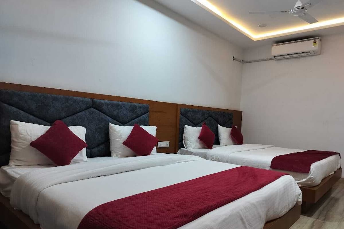 Ein Hotelzimmer mit zwei Betten, jeweils mit weißer Bettwäsche und roten Ziertelementen, einem Holz-Kopfteil und einer Klimaanlage an der Wand.