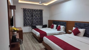 Une chambre d’hôtel avec deux lits, un bureau avec un ordinateur, un ventilateur de plafond et une fenêtre avec des rideaux à motifs.