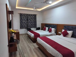 Habitación de hotel con dos camas, un escritorio con computadora, un ventilador de techo y una ventana con cortinas estampadas.