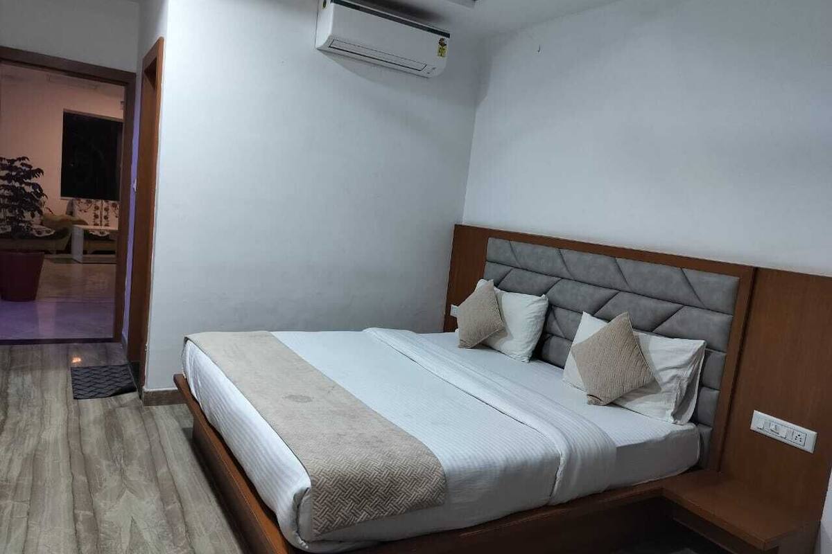 Ein ordentlich bezogenes Bett mit grauem Kopfteil, einem Nachttisch und einer an der Wand montierten Klimaanlage.