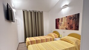 Habitación de hotel con dos camas, un televisor de pantalla plana montado en la pared, un cuadro en la pared y una cortina.