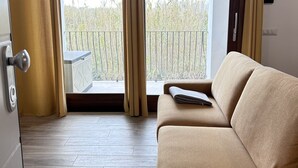 Una habitación con sofá, ventana con cortinas, vista a un balcón y puerta con picaporte.