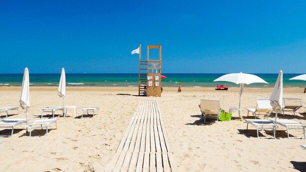 A beach with a wooden walkway leading to the sea, white beach chairs, and umbrellas. - Cozy home in Marina di Modica with house sea view (Marina di Modica)