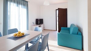 A modern living room with a dining table, blue chairs, a teal sofa, a TV on a stand, and a door leading outside. - Cozy home in Marina di Modica with house sea view (Marina di Modica)