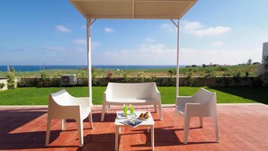 A covered outdoor seating area with white chairs and a table, overlooking a grassy landscape and the sea. - Cozy home in Marina di Modica with house sea view (Marina di Modica)