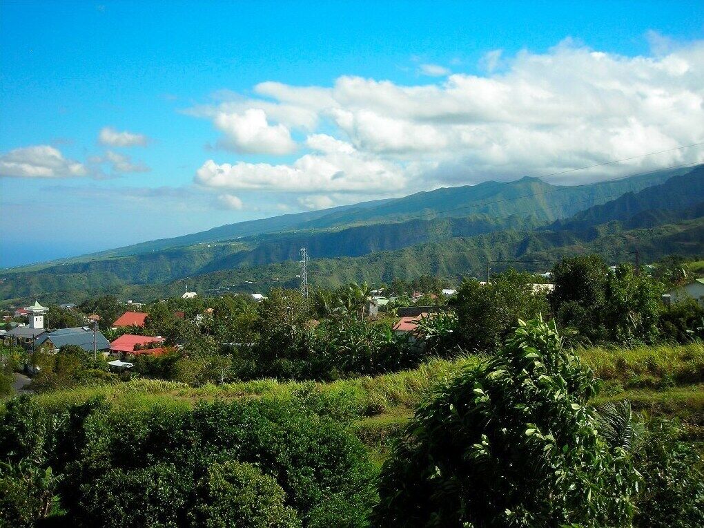 A rural landscape with a small village, houses with red roofs, and lush green hills in the background.
