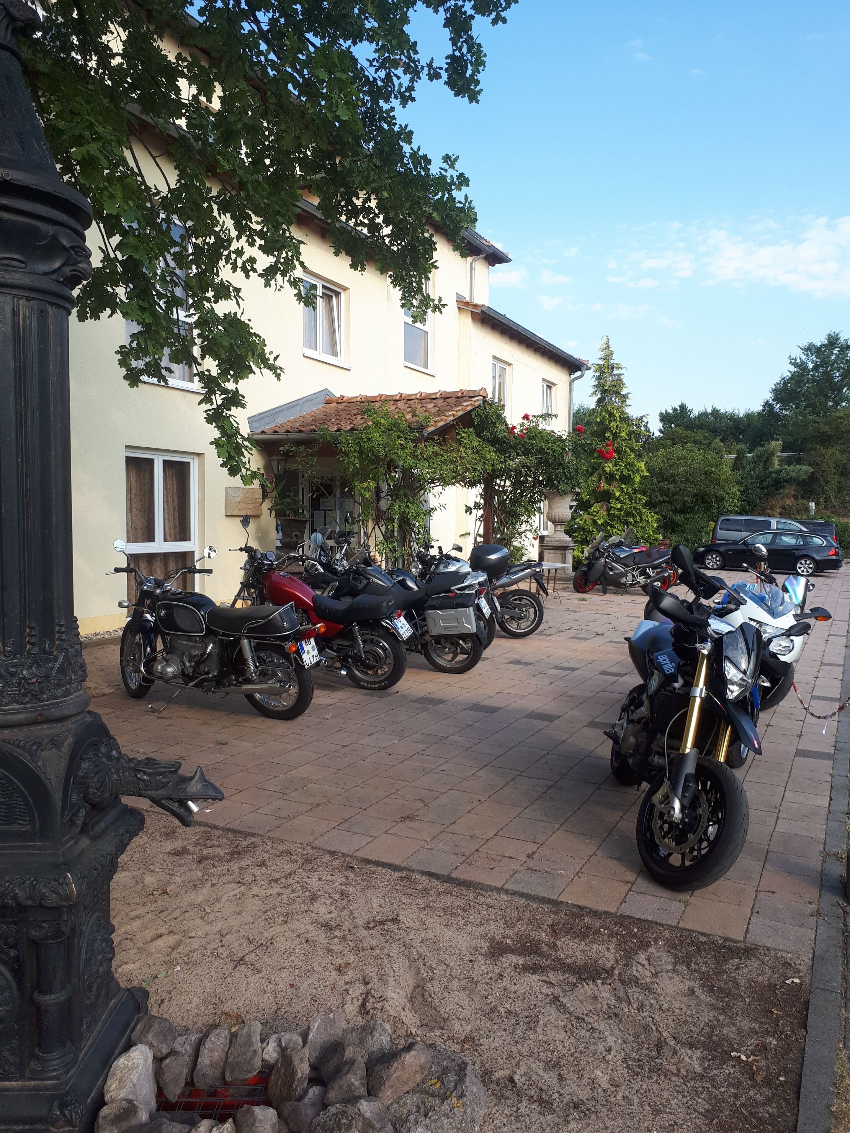 A row of parked motorcycles in front of a building with a tiled roof and a stone column.