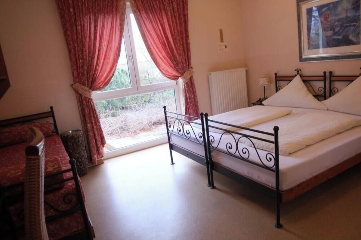 A bedroom with a bed, a window with curtains, a radiator, and a framed picture on the wall.