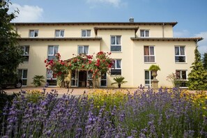 A two-story building with a symmetrical facade, multiple windows, and a central entrance with a decorative arch. - Mediterran Hotel Juwel (Karlstein am Main)