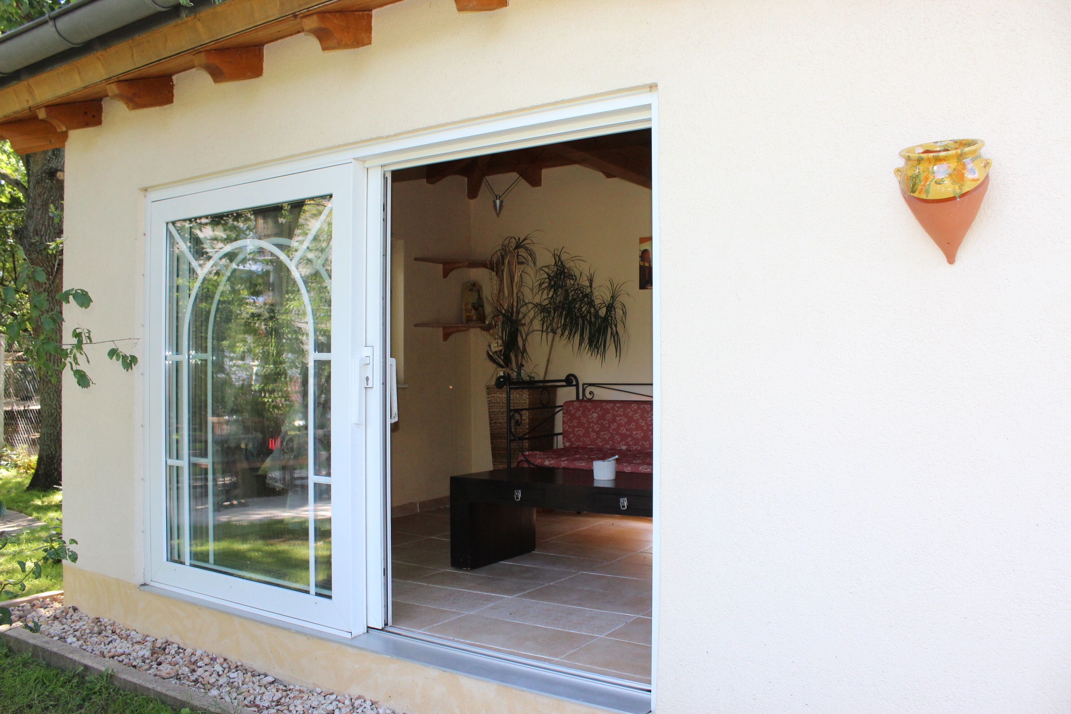 A room with a sliding glass door leading to an outdoor area, a small table with a chair, and a potted plant.