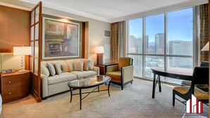 Habitación de hotel moderna con un ventanal grande que ofrece vistas a la ciudad, un sofá, una mesita de café y una silla.