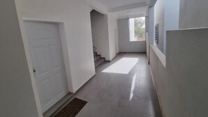 A narrow hallway with white walls, a door on the left, and a window at the end.