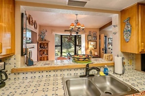 Una cocina con un lavamanos doble, armarios de madera, un bol decorativo en la encimera y una lámpara de araña.