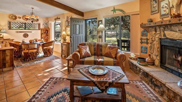 A cozy living room with a fireplace, a dining area with a wooden table and chairs, and a large window with a view of the outdoors.