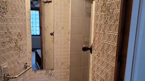 Een badkamer met patroon betegelde vloertegels, een handgreep, een douchegedeelte en zicht op een andere kamer.