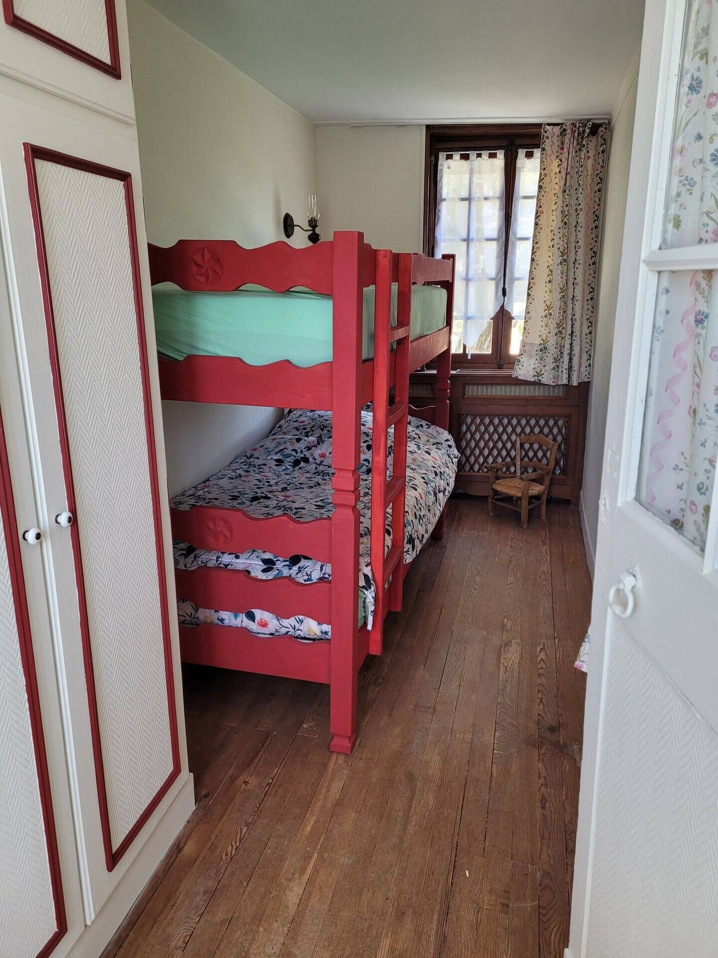 A room with three bunk beds, a wooden desk, and a window with floral curtains.