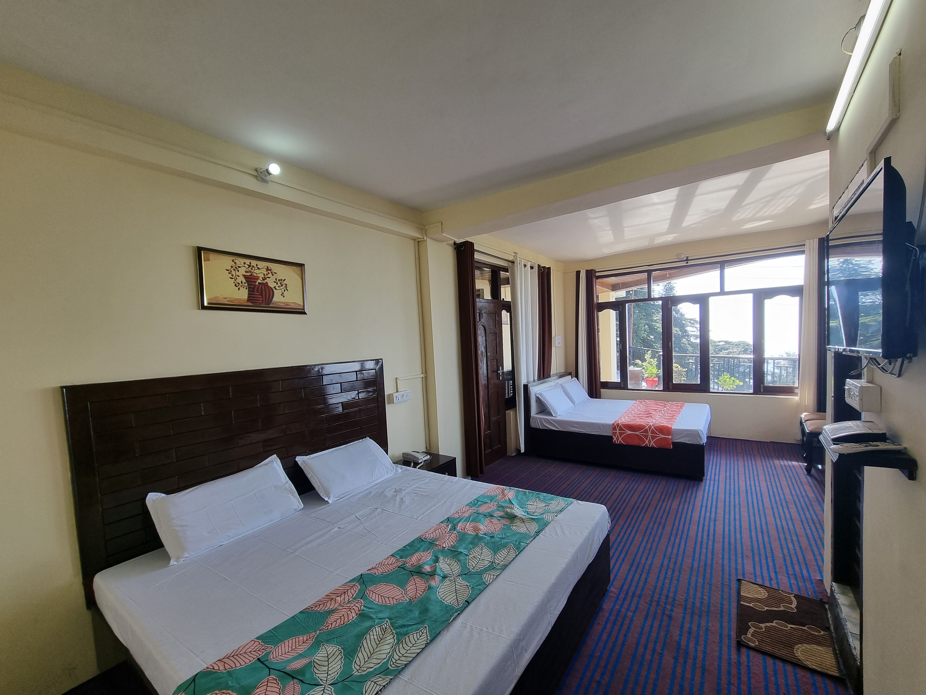 Habitación de hotel con dos camas, un ventanal grande, un televisor y un cuadro enmarcado en la pared.